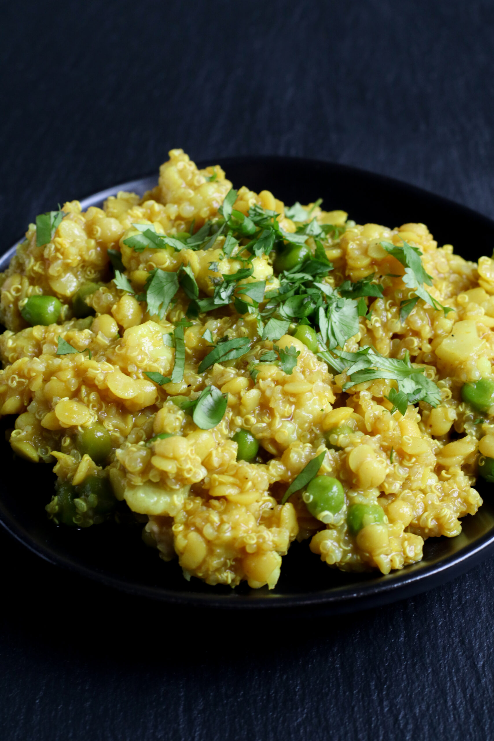 black plate filled with quinoa kitchari and topped with cilantro